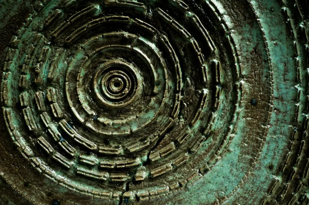 Pièce de bronze patiné vert-de-gris ornée de cercles concentriques en relief.