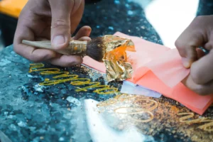 Pose de la feuille d’or au pinceau sur des lettres gravées dans un granit sombre.